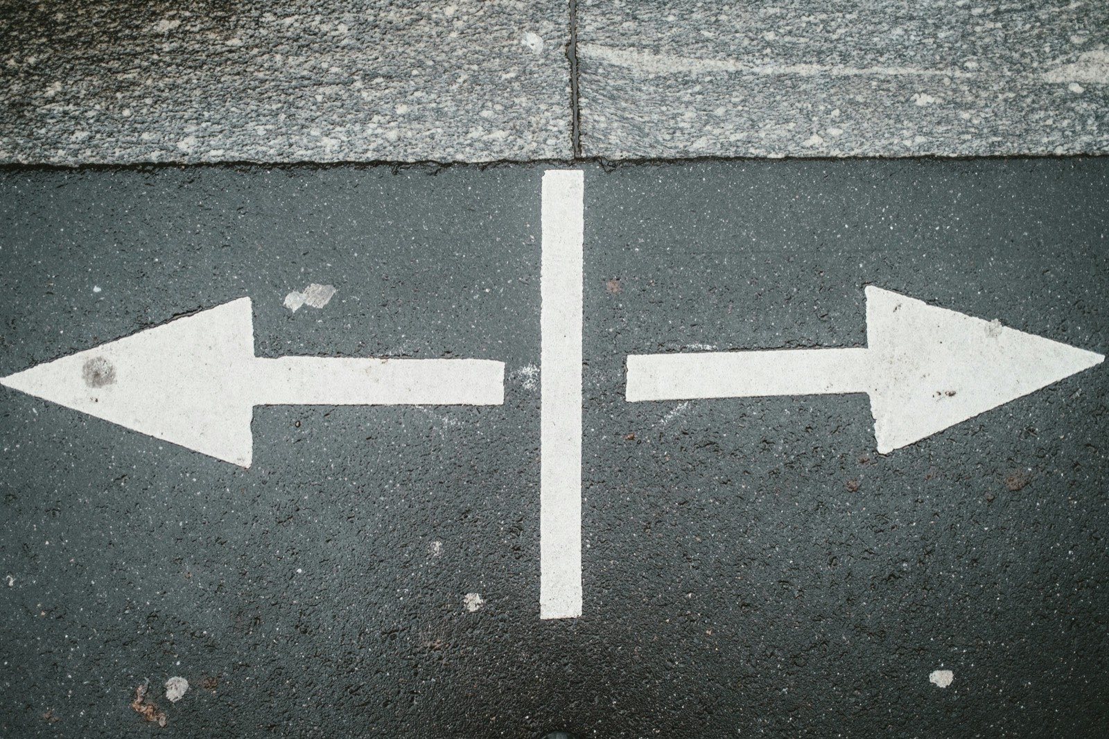 Two white arrows painted on tarmac pointing in opposite directions, left and right.